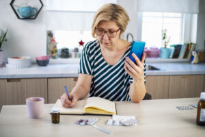 Mature woman using smart phone for conversation with her doctor. She is sitting at her kitchen table and notes doctors advice.